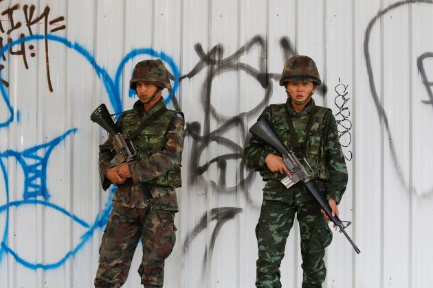 Thai soldiers take their position in front of a wall with graffiti in central Bangkok