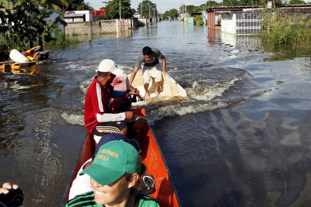 A man in a styrofoam box (C) is towed by a raft in a flooded street in Guasdualito