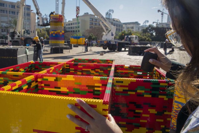 A woman assembles bricks as she works on a component of a LEGO tower under construction in Tel Aviv's Rabin Square on December 26, 2017, as the city attempts to break Guinness world record of the highest such structure. / AFP PHOTO / JACK GUEZ