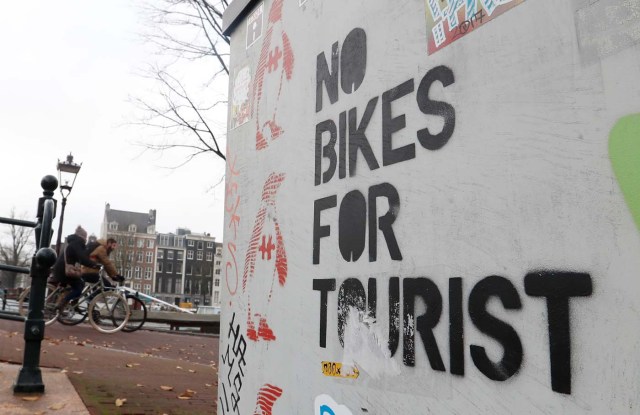 Cyclists ride past a graffiti reading "no bikes for tourist" in central Amsterdam, Netherlands, December 1, 2017. REUTERS/Yves Herman