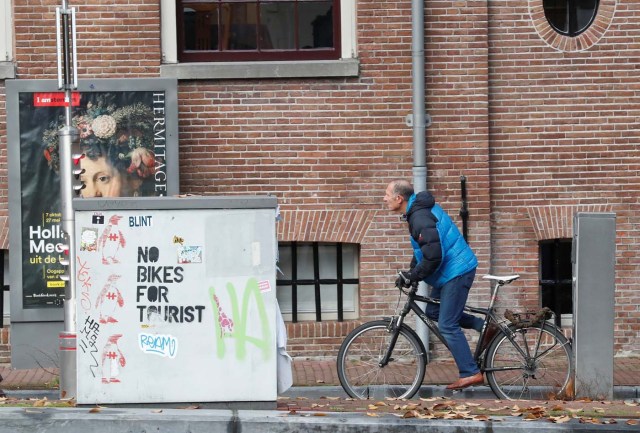 A cyclist rides past a graffiti reading "no bikes for tourist" in central Amsterdam, Netherlands, December 1, 2017. REUTERS/Yves Herman