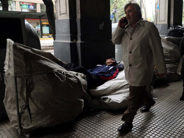 A garbage recycler sleeps over sacks of recyclables as a man walks by in Buenos Aires' financial district, Argentina May 9, 2018. REUTERS/Marcos Brindicci